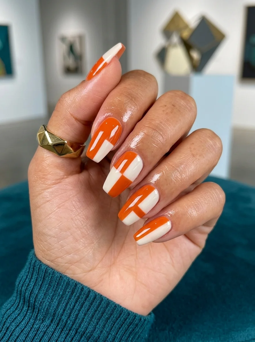 Long coffin nails with bold geometric color blocking in bright orange and white in diagonal and rectangular patterns.