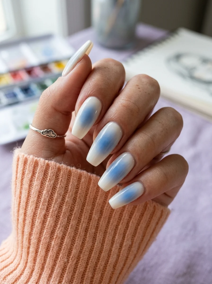 Long almond nails with a milky white base and soft blue watercolor cloud effect in the center.