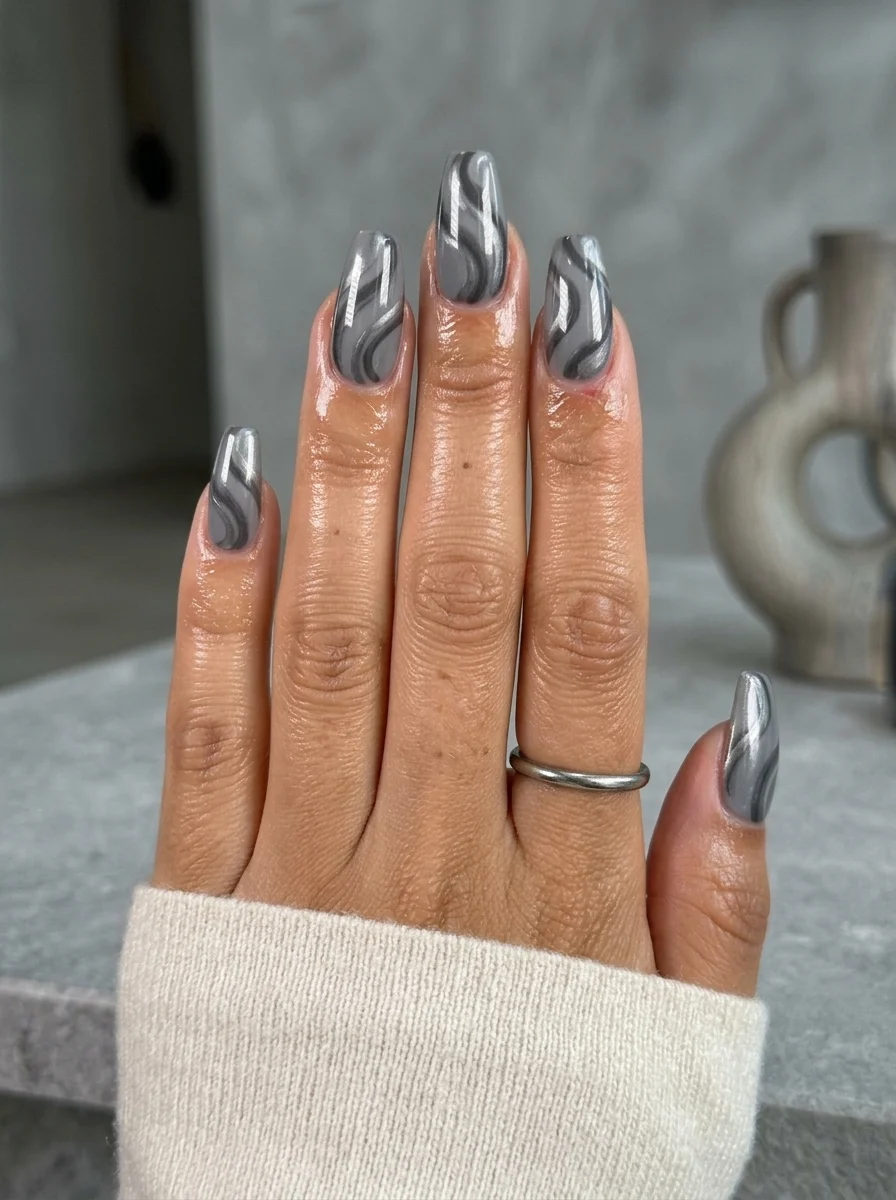 Long stiletto nails with a grey chrome finish and dark swirl patterns creating a marble-like effect.