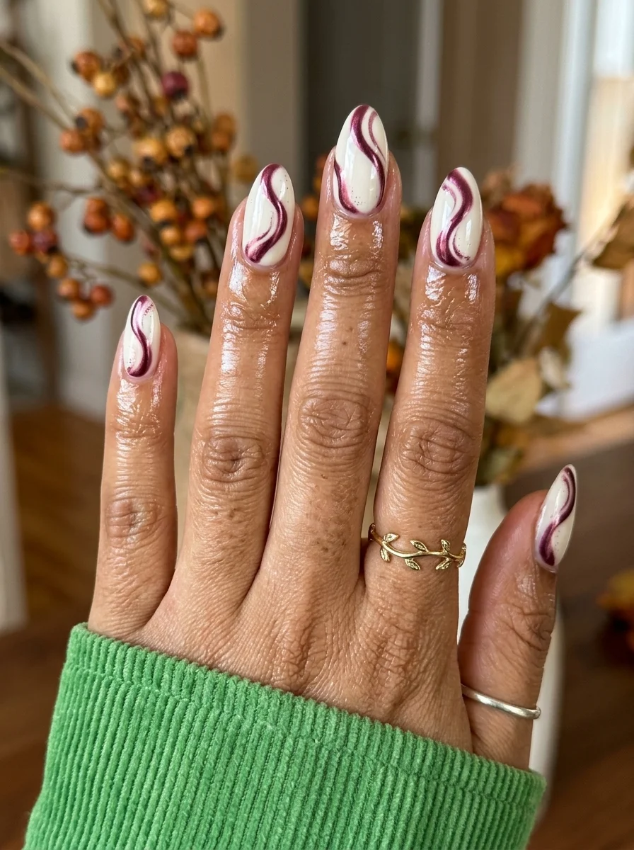 Almond nails with a white base and deep burgundy swirl designs flowing across each nail.