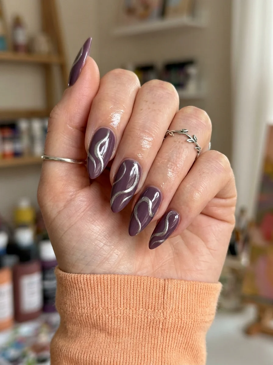 Almond nails with a dusty plum purple base and silver metallic swirl designs.