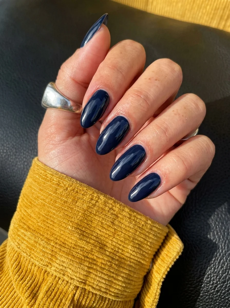 Almond nails with a deep navy blue glossy solid color polish.