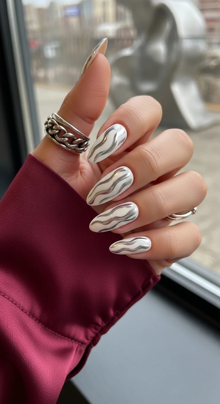 Almond nails with white base and silver chrome wavy swirls.