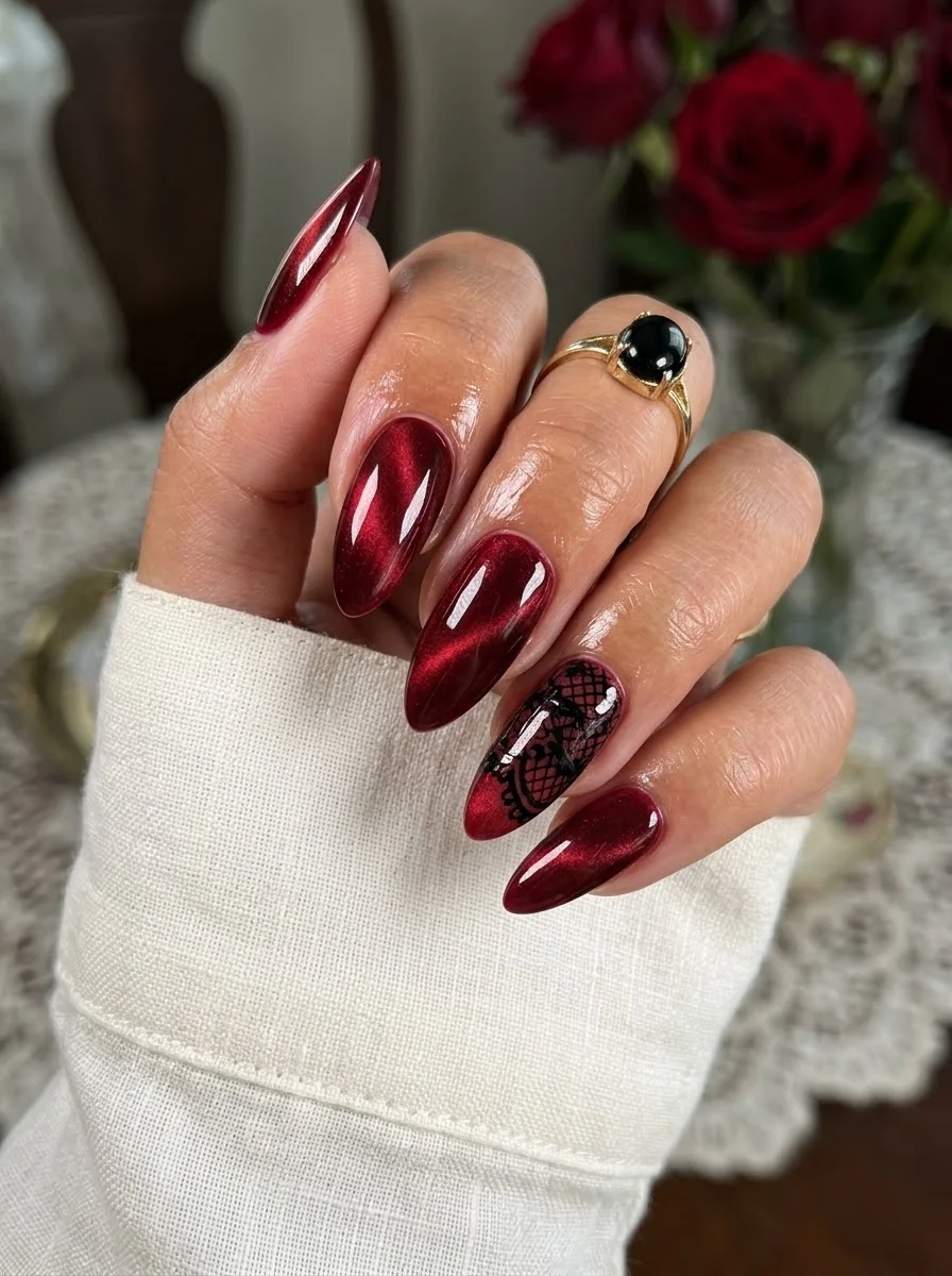 Deep red cat-eye almond nails with a black lace accent on the ring finger.
