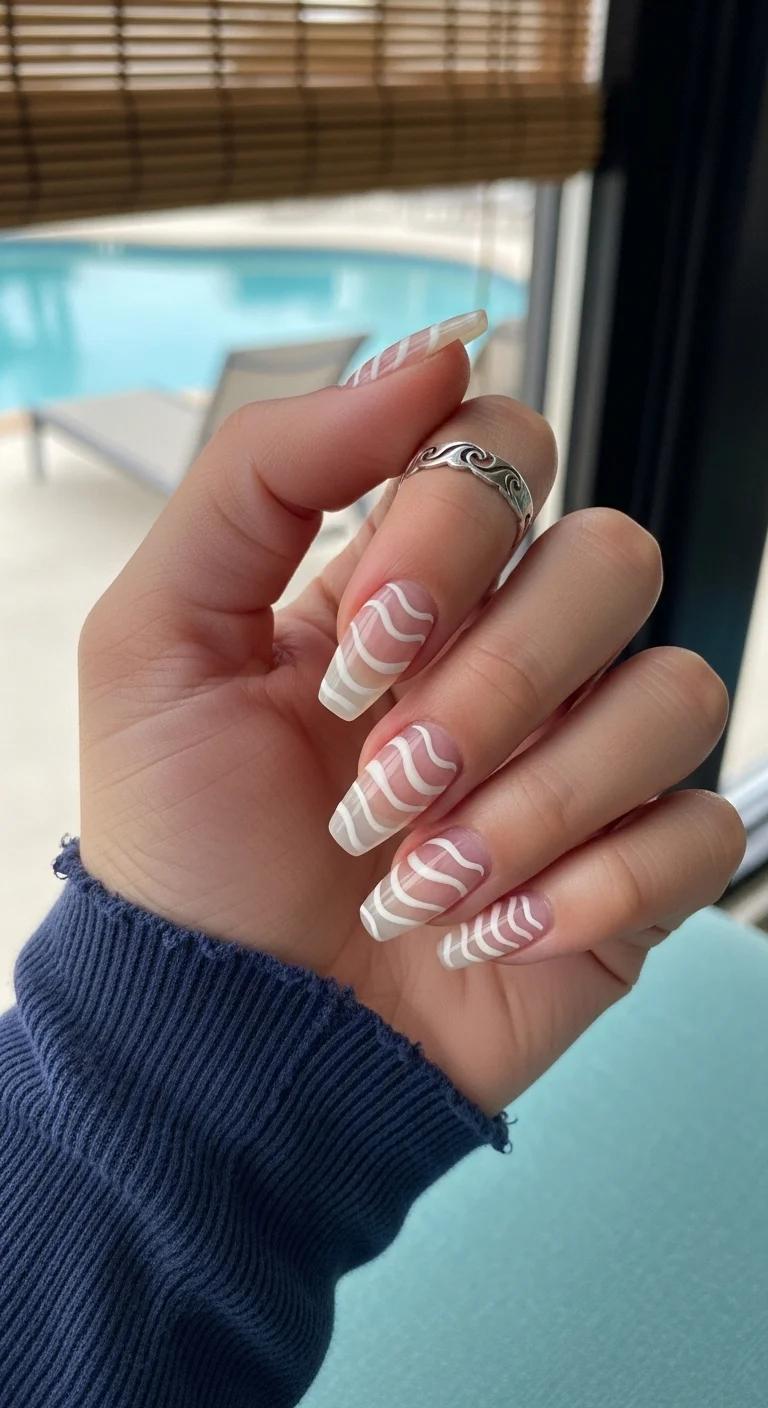 Long coffin nails with a sheer nude base and white swirl patterns resembling marble veins.