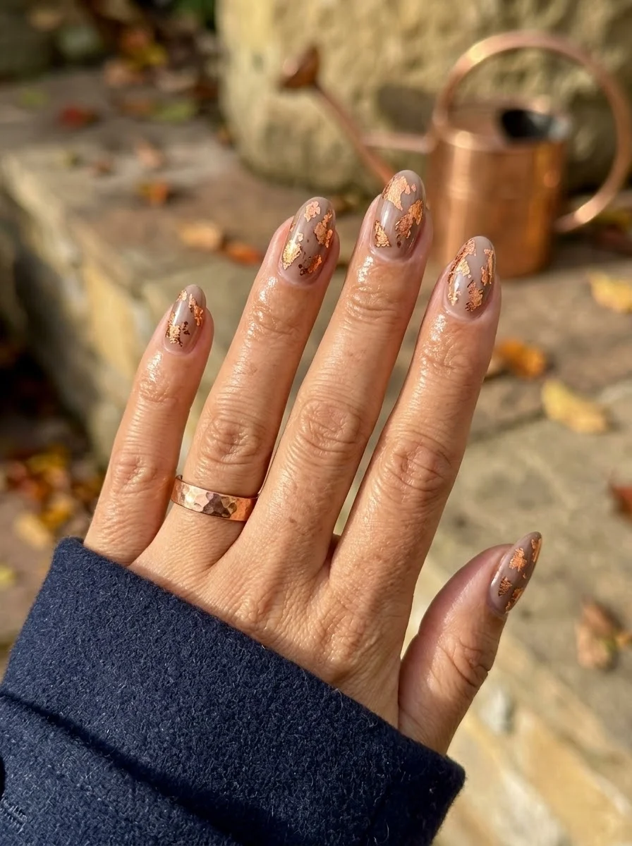 Medium almond nails with sheer nude base and copper leaf fragments scattered across each nail.