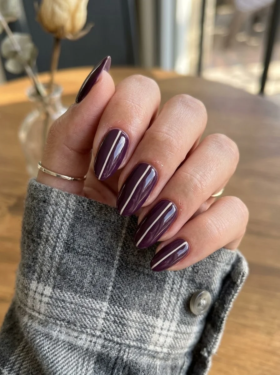 Medium oval nails with deep burgundy base and thin white vertical pinstripe down the center.