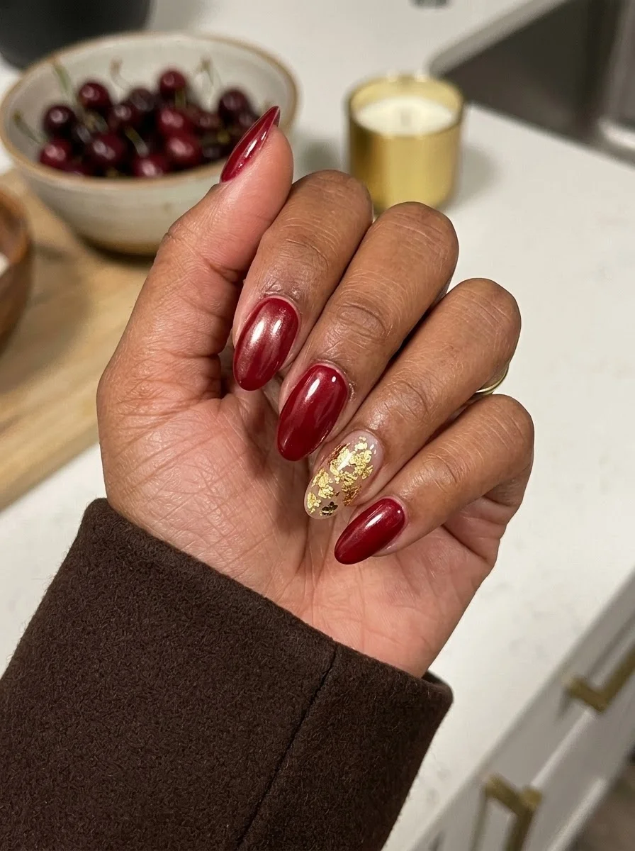 Medium oval nails with deep cherry red polish and gold leaf accent on the ring finger.