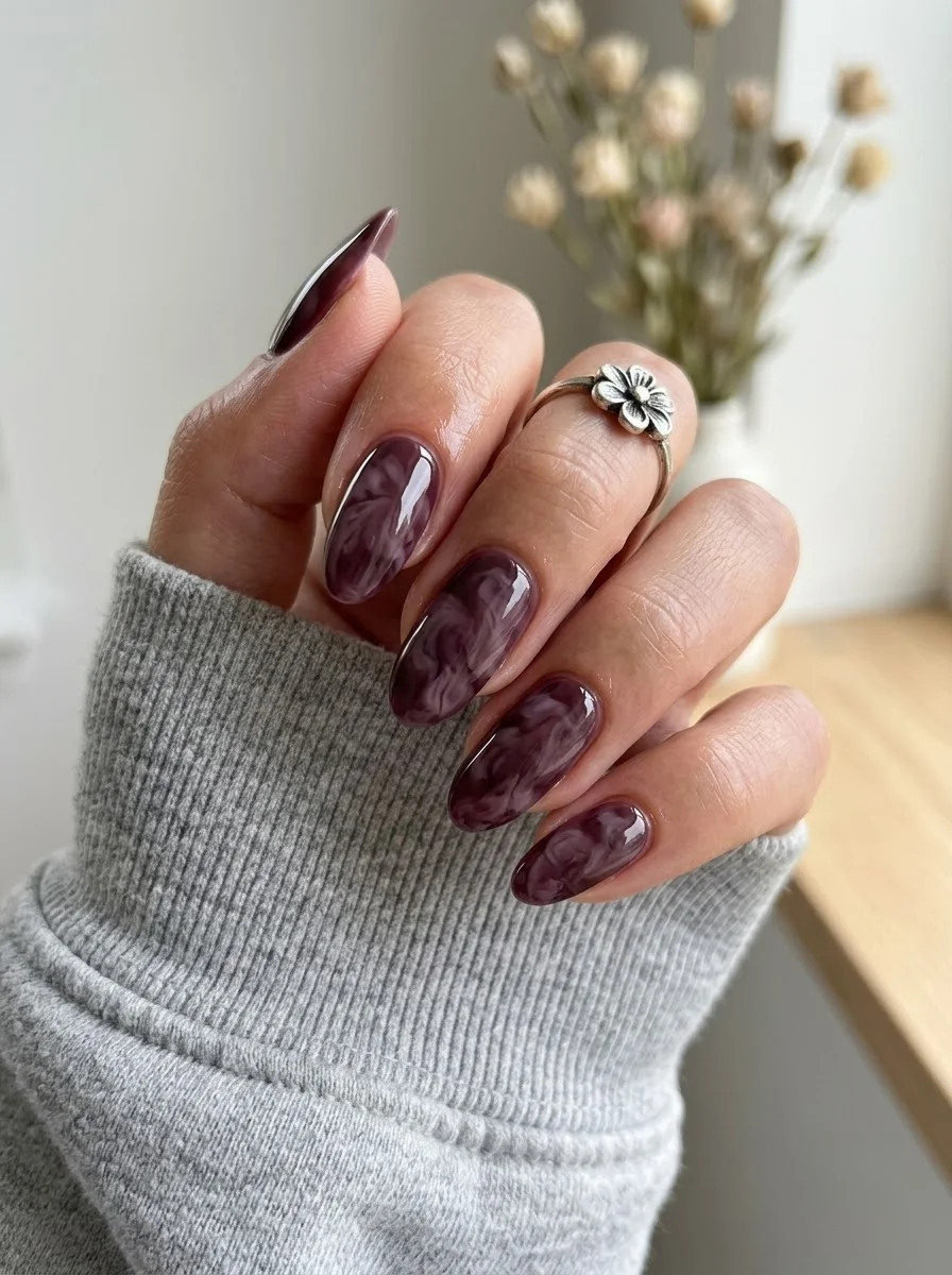 Medium oval nails with dark purple base and white marble swirl pattern.