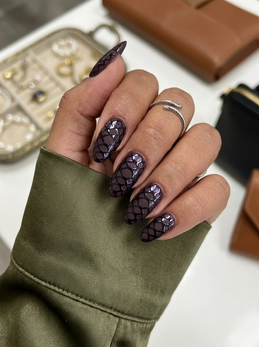 Medium oval nails with dark purple base and snakeskin or reptile scale pattern with glitter.