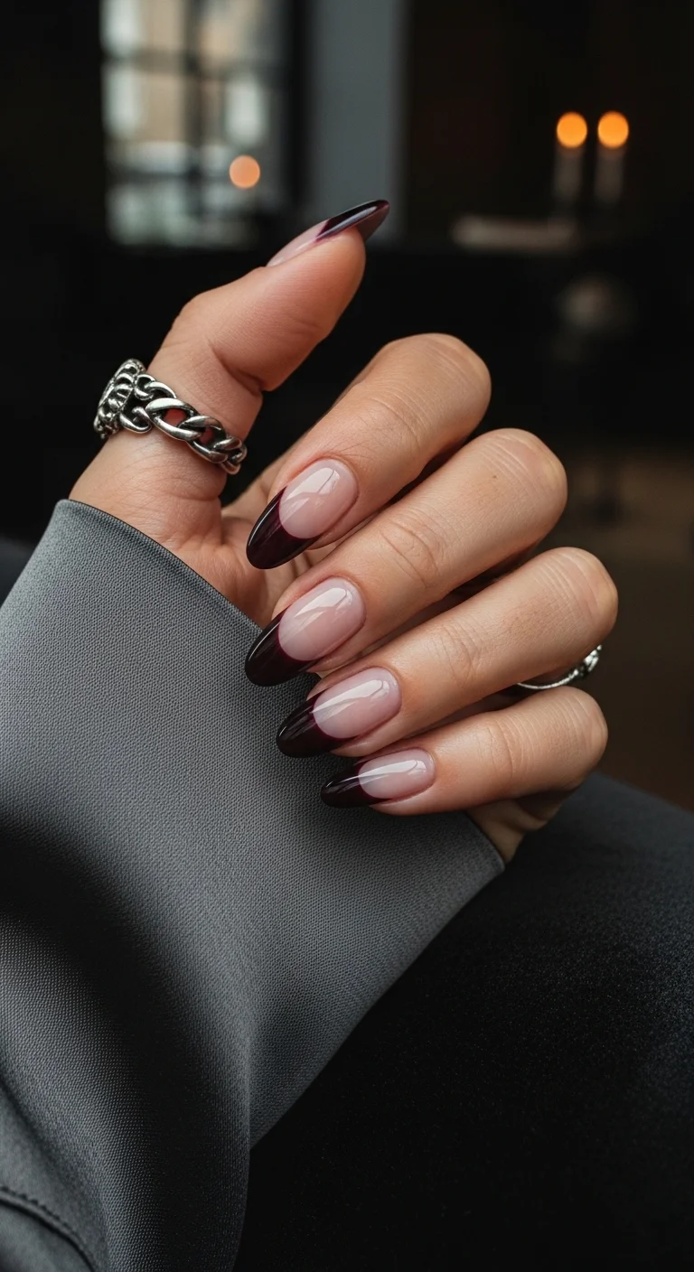 Almond nails with a nude base and deep burgundy/black French tips.