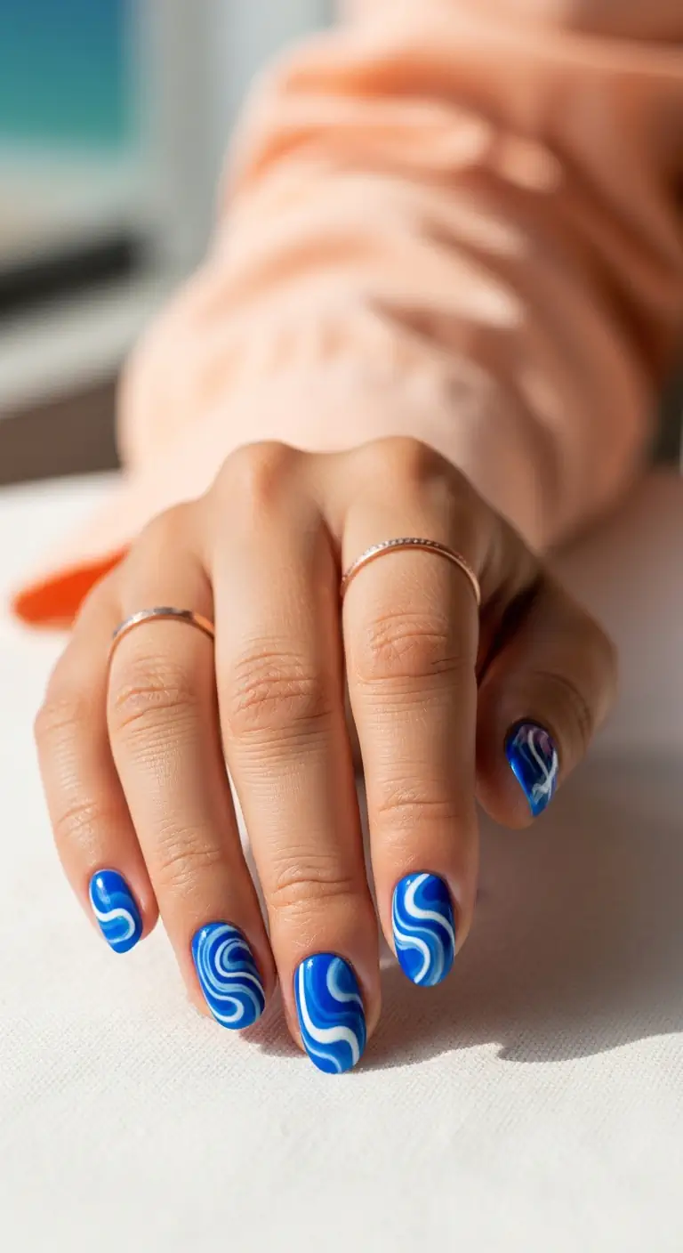 Vivid cobalt blue short oval nails decorated with abstract white and light blue swirls