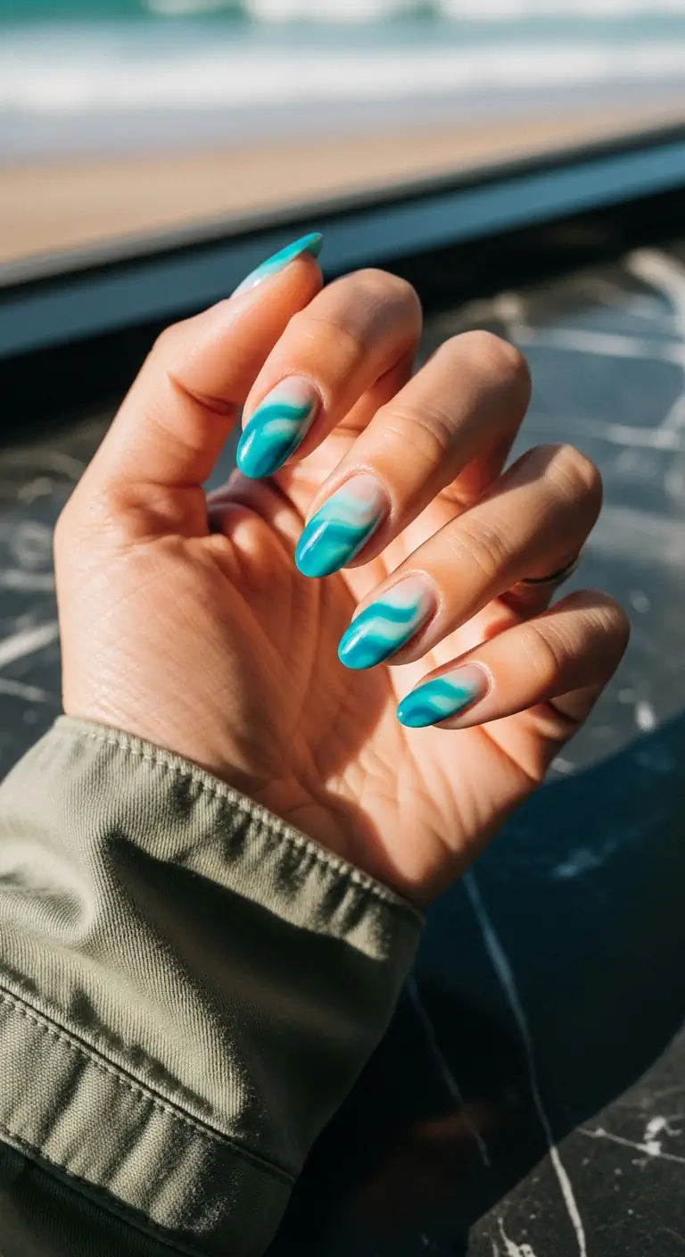 Short oval nails with a sheer nude base and fluid, layered teal and turquoise wave art at the tips