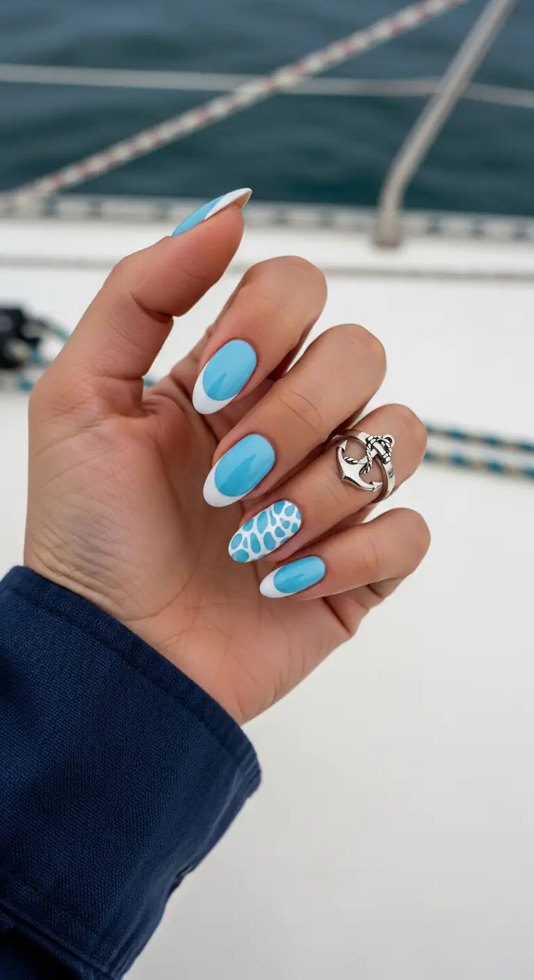 Medium length oval blue nails with classic white French tips on some nails and detailed blue-on-white animal print on the ring finger, styled on a boat