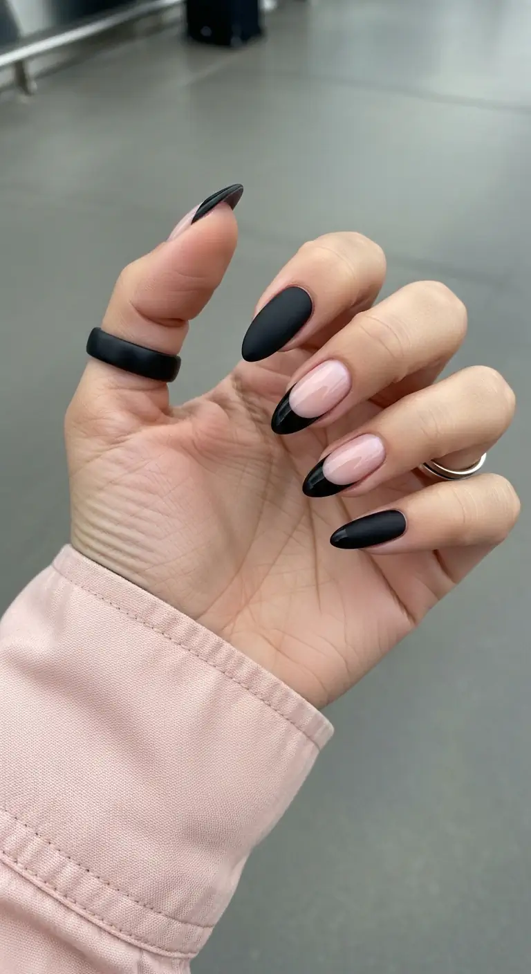 Medium oval nails with alternating full matte black and matte black French tips on a clear base, styled against a blurred airport interior