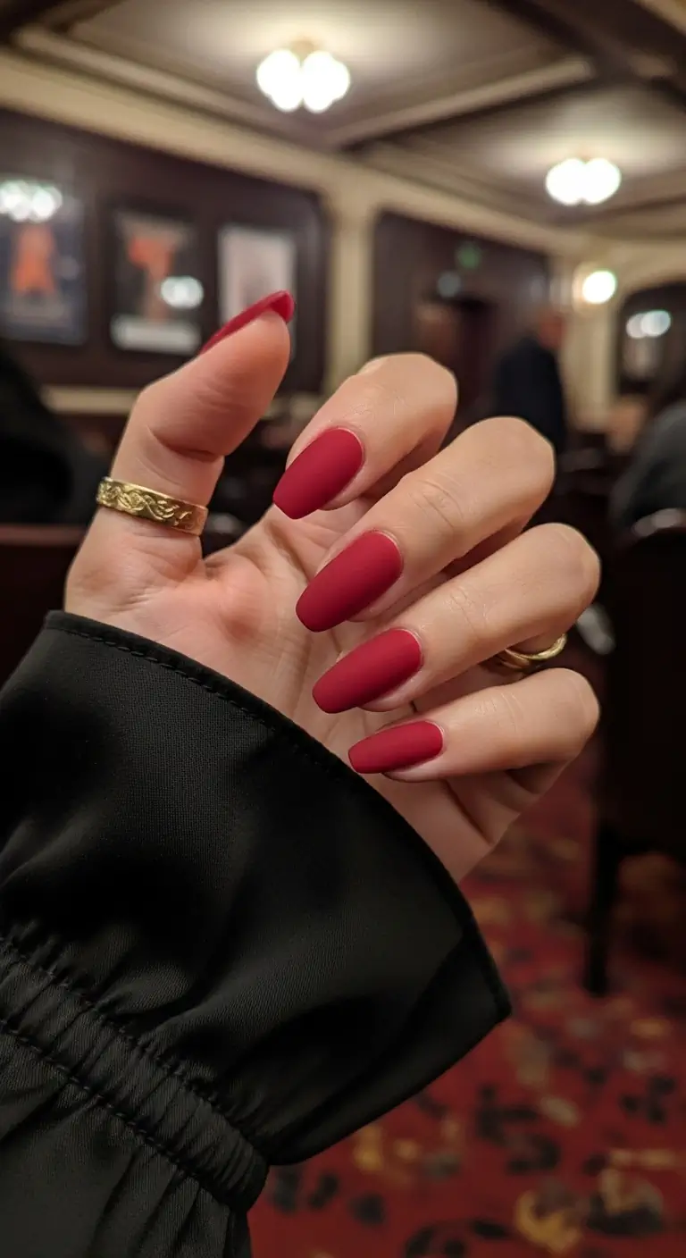 Long, clean matte crimson red coffin nails set against a blurred opulent theatre lobby